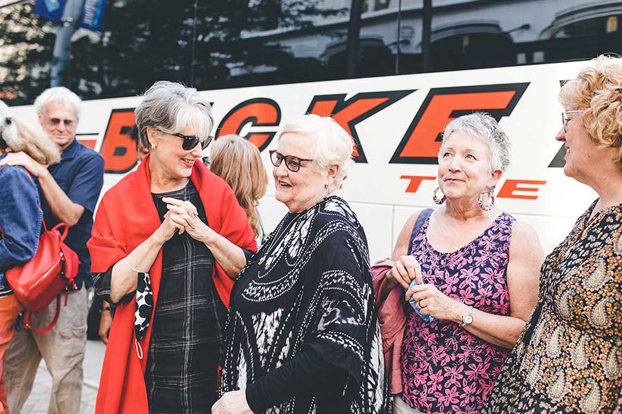 A group of teachers with Muse staff members, smiling and laughing in front of a bus