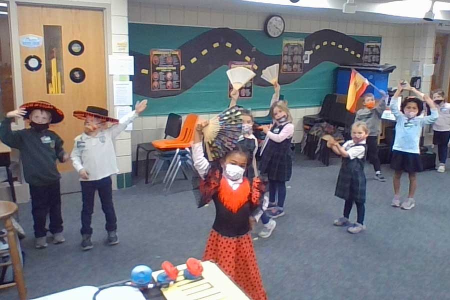 Many elementary school students in their classroom, wearing multicultural costume pieces, waving flags and decorative fans