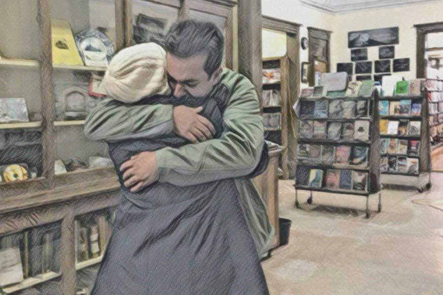 A man and a woman, both wearing coats, hug in a library
